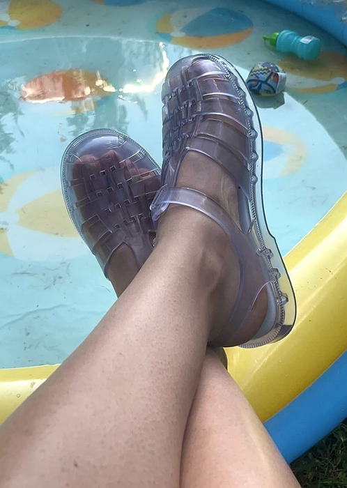 Person wearing clear jelly sandals, with their feet resting on the edge of a small inflatable pool