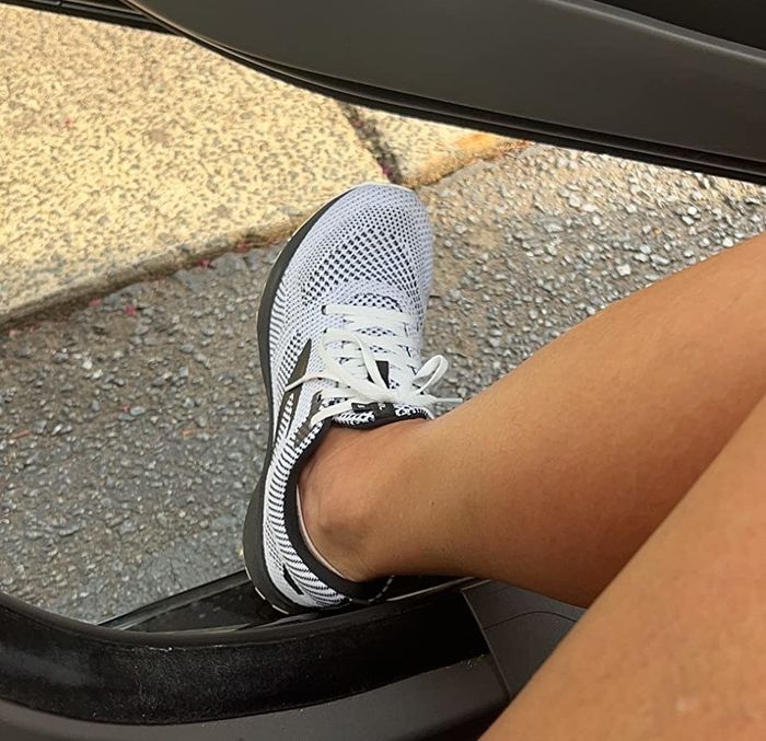 The reviewer steps out of the car wearing white and black shoes.