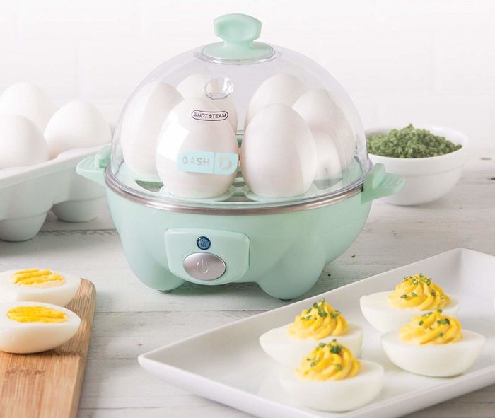 The aqua-colored egg cooker with a clear dome lid and a prominent power button on the front
