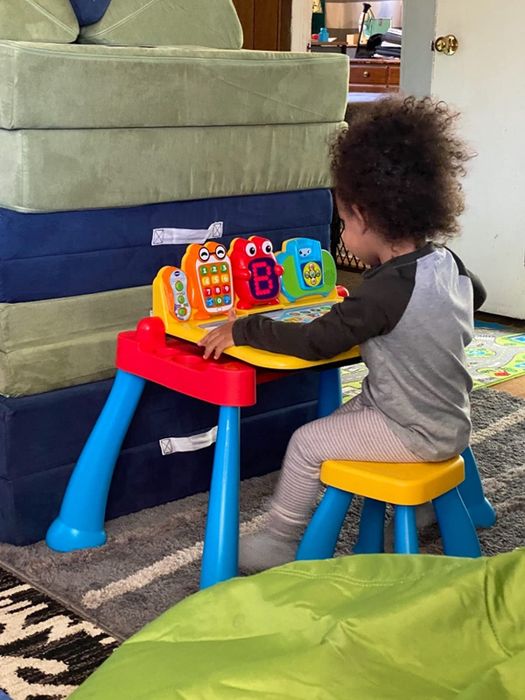 A child sitting on a stool, engaged in play at an activity desk.