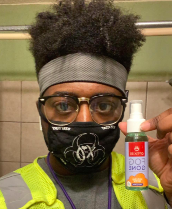 A reviewer's photo featuring them holding a bottle of anti-fog spray, wearing a cloth mask and glasses that remain fog-free.
