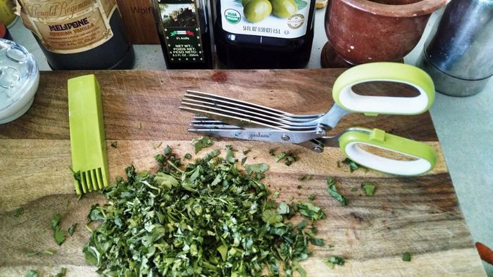 A reviewer's photo of a cutting board displaying neatly chopped herbs alongside a pair of herb scissors.