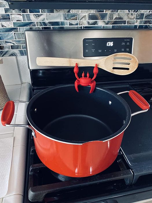 a photo from a reviewer showing the silicone crab spoon rest gripping a wooden spoon while attached to a red pot
