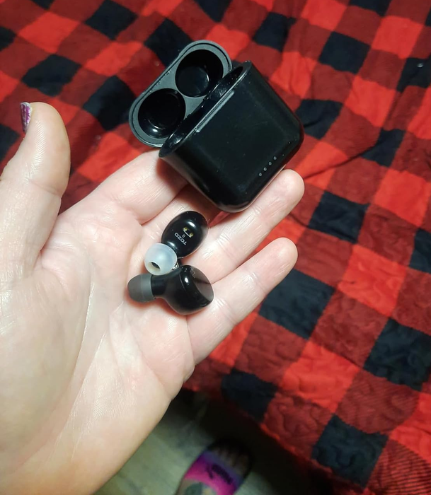 A reviewer holding the earbuds in one hand, with the case in the other