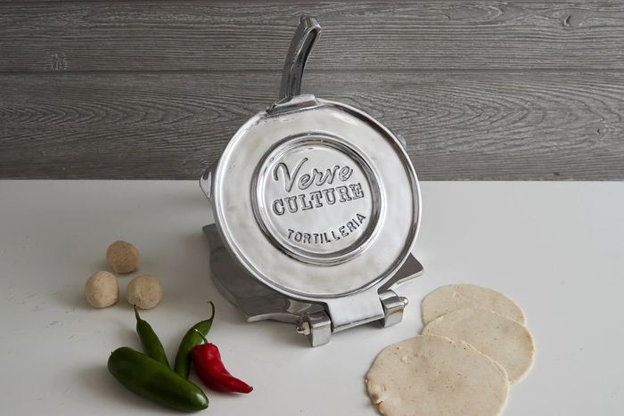 A vibrant red tortilla maker with dough balls and freshly pressed tortillas beside it