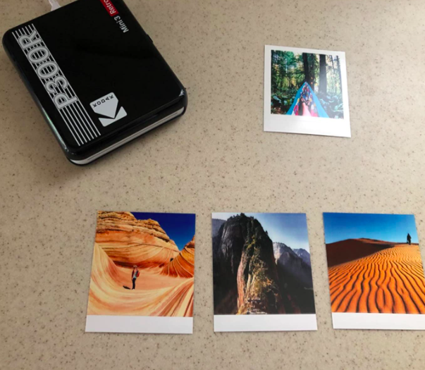 A reviewer's photo showing the portable printer alongside four printed photos.