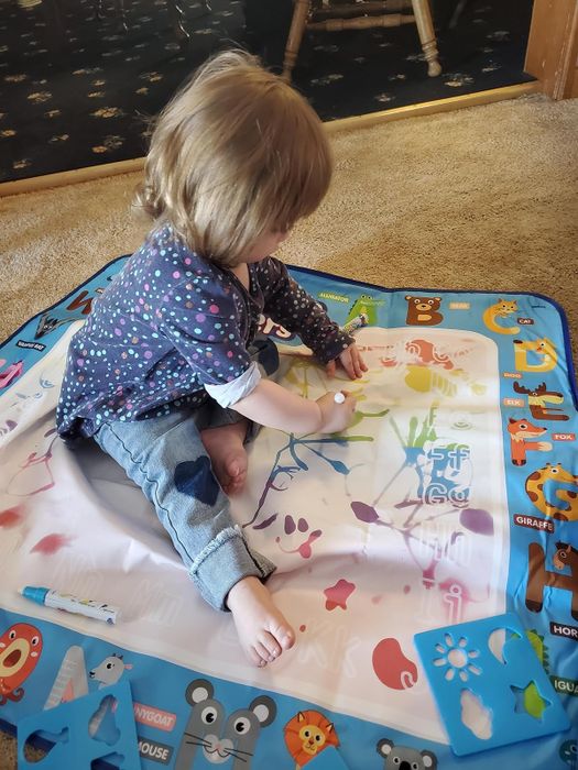 A child seated on the floor, actively drawing on the doodling mat.