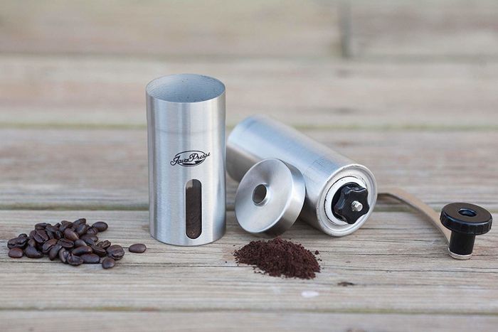 The grinder is depicted amidst a scattering of coffee beans, showcasing both the whole beans and the fine grounds it produces.