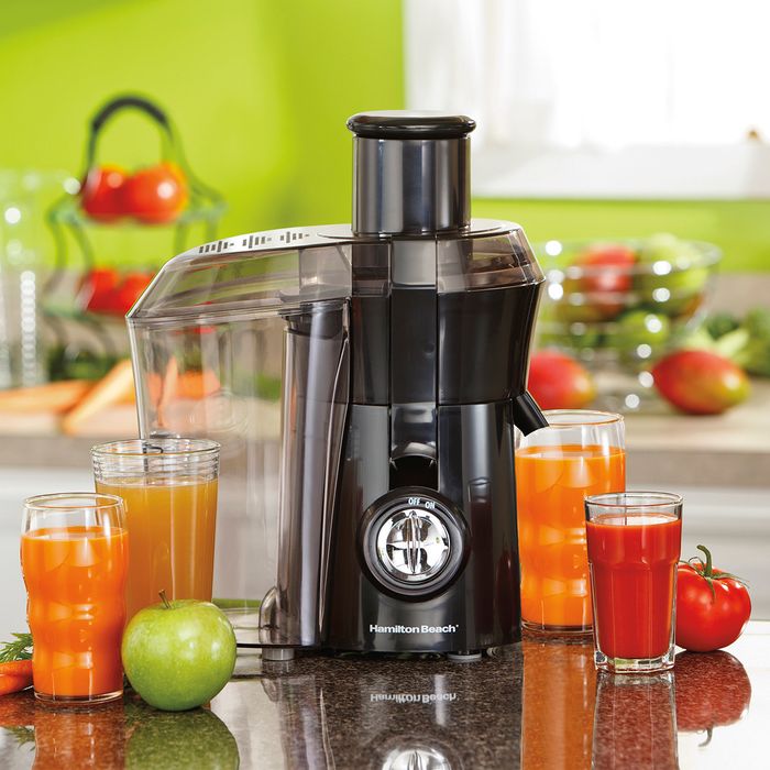 A juice extractor placed on a countertop, surrounded by various cups filled with different types of juice, alongside fresh apples and tomatoes.