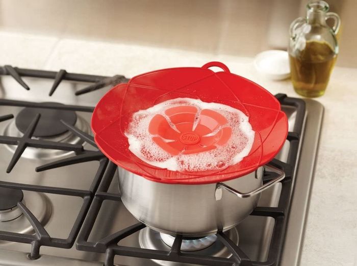 A red spill stopper sits atop a pot on a stove, with boiling water inside, demonstrating its ability to prevent boil-overs.