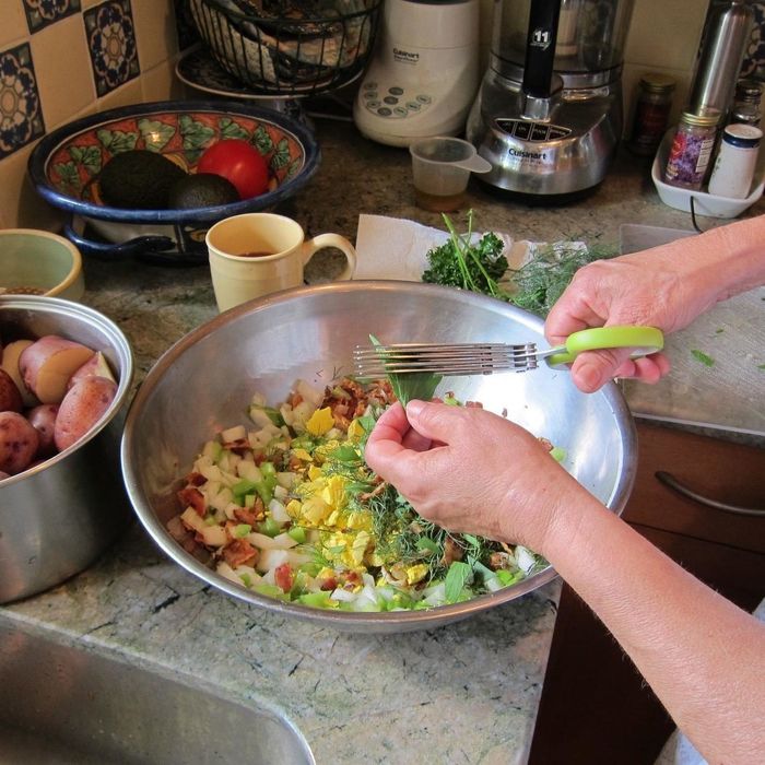 A reviewer's photo showcasing the process of cutting fresh herbs over a bowl filled with salad ingredients.