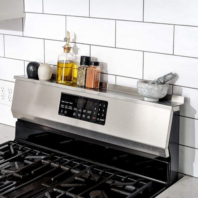 A stainless steel shelf mounted on the back of a stove, holding oil bottles, salt and pepper shakers, assorted spices, and a mortar and pestle.