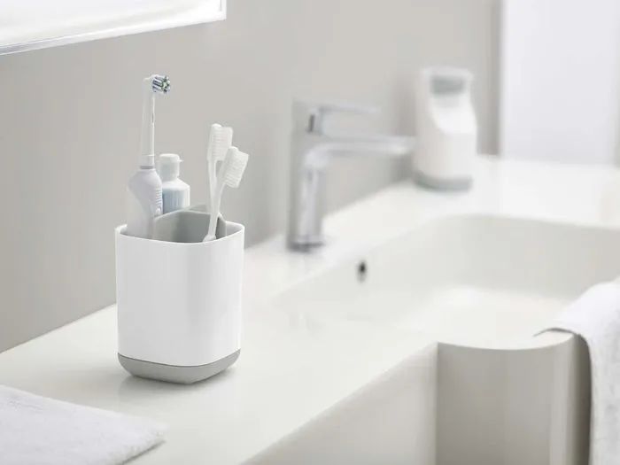 A caddy with three sections holding two manual toothbrushes, an electric toothbrush, and a toothpaste tube