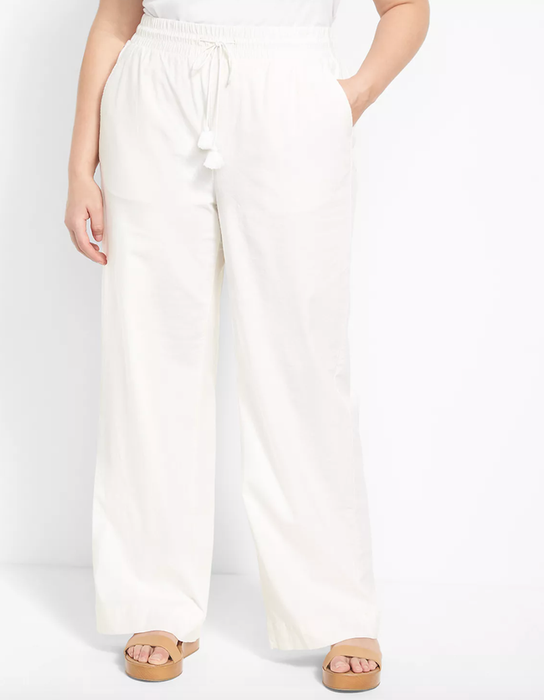 The model is wearing white linen pants and tan platform sandals.
