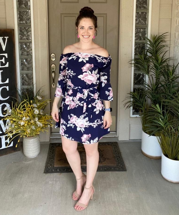 The reviewer is seen wearing a blue floral dress, exuding a fresh and feminine vibe.