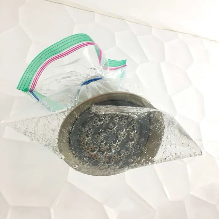 a shower head wrapped in a plastic bag filled with liquid, secured with a rubber band