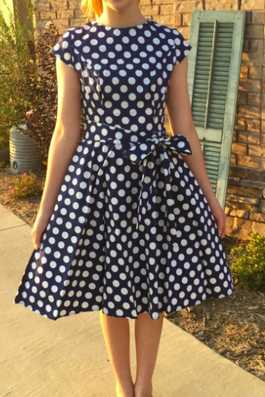 The reviewer models the blue dress adorned with classic white polka dots, offering a playful yet sophisticated look.