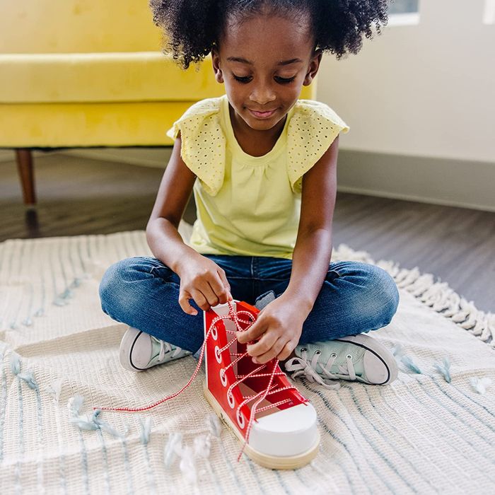 A child practicing tying shoes on a big red shoe learning toy, perfecting their skills.