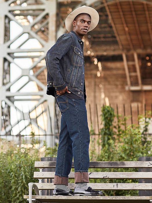 A model wearing a cowboy hat and straight-leg jeans, standing on a bench