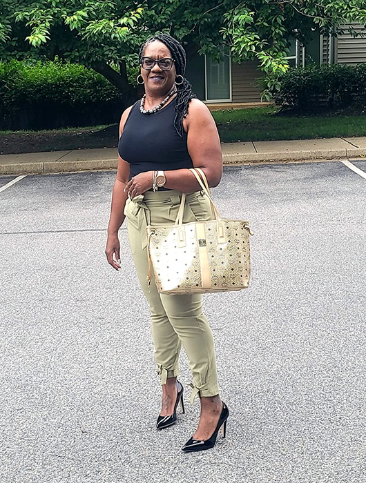 The reviewer is dressed in a black top and pale green high-waisted tie-knot pants.
