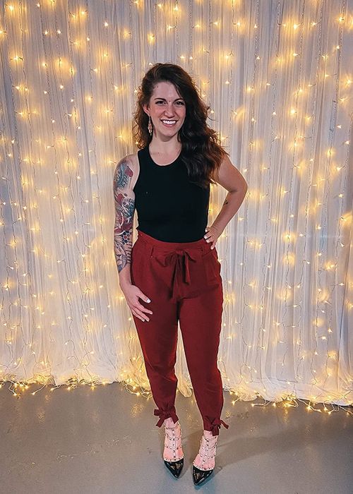 The reviewer is wearing a black top and maroon high-waisted tie-knot pants.