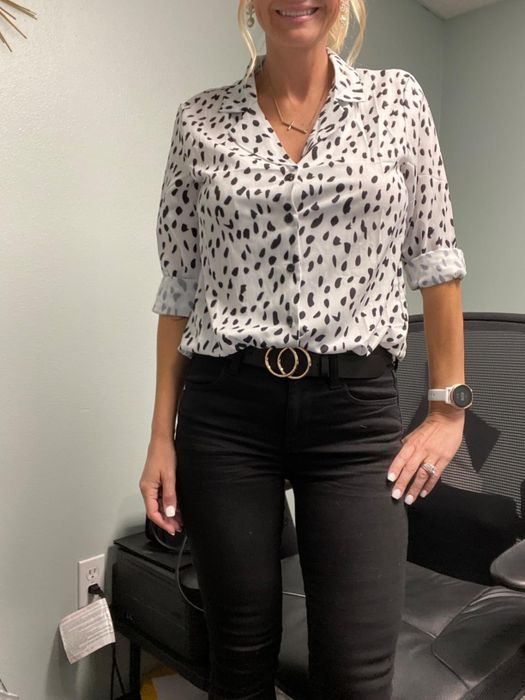 A reviewer is wearing a white button-down top with black speckles, matched with black pants