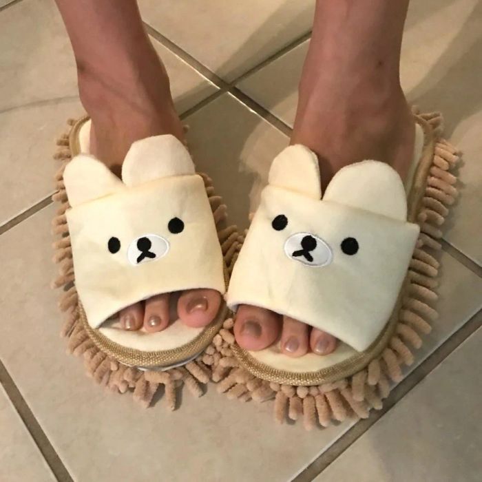 reviewer wearing slippers with teddy bear designs on top and short, fuzzy mop-like fibers covering the soles