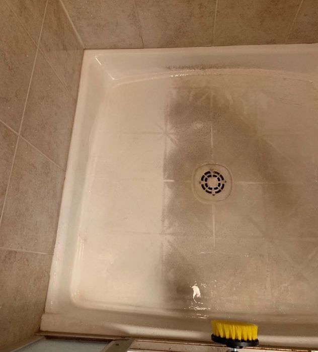 A photo from a reviewer showing a shower stall with dirty marks, partially cleaned, and a scrub brush resting nearby
