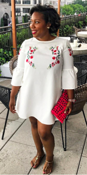 The reviewer is seen wearing the white mini dress featuring vibrant red floral embroidery, adding a pop of color to their look.