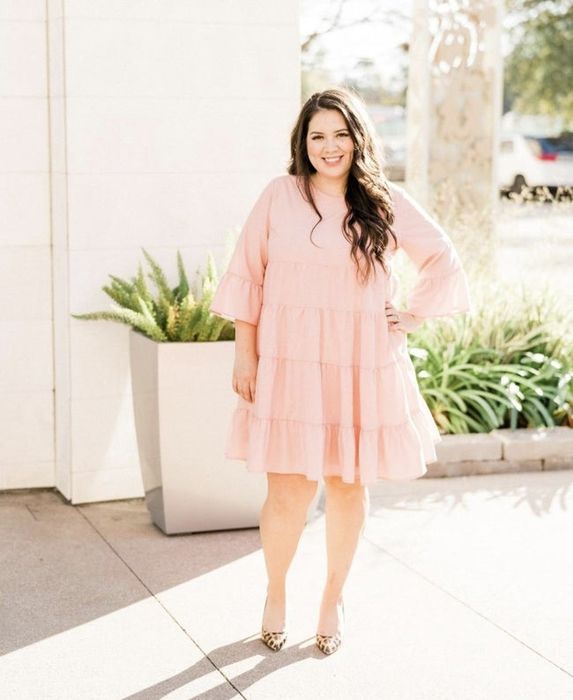 The reviewer is wearing a pink tiered dress with leopard print heels.