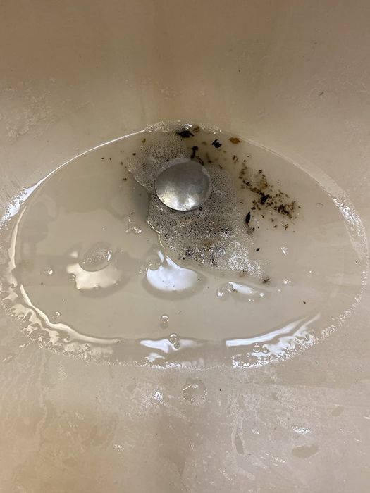 On the right, the same sink displays black residue flowing out of the drain after applying the cleaner.