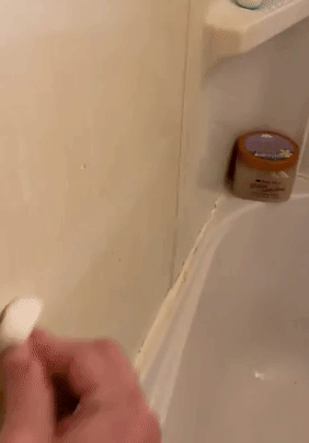 A reviewer using a white sponge to clean a shower wall