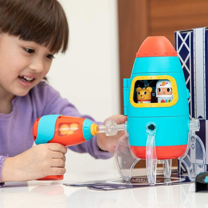 A child enthusiastically using a plastic toy drill to assemble a colorful rocket ship, sparking creativity and learning in the process.