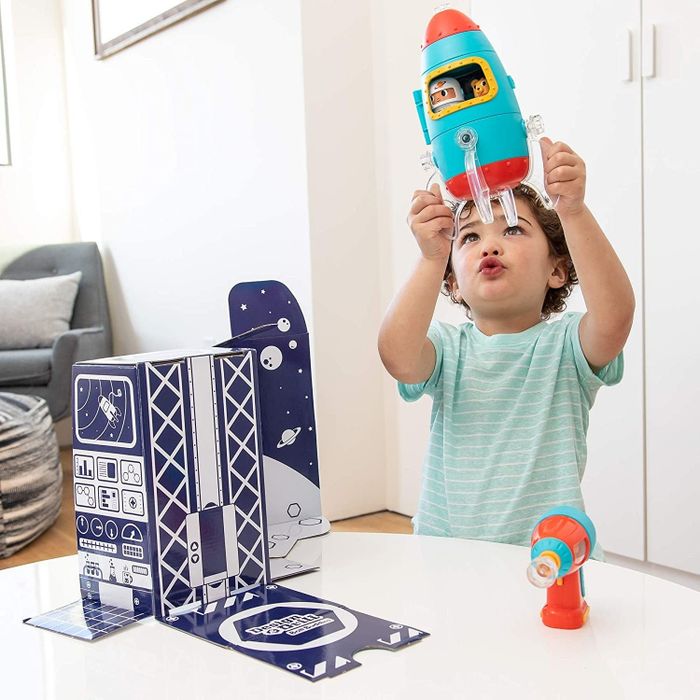A child is shown with the packaging of a set of primary-colored rocket ships and a launch pad, ready to embark on a space adventure.