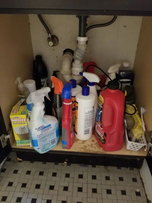 photo showing a cluttered cabinet under a sink filled with cleaning supplies and toiletries