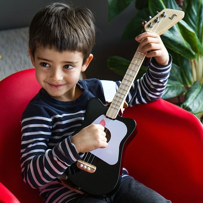 A child playing on a toy guitar, which is strapped around them, looking like a mini rock star.