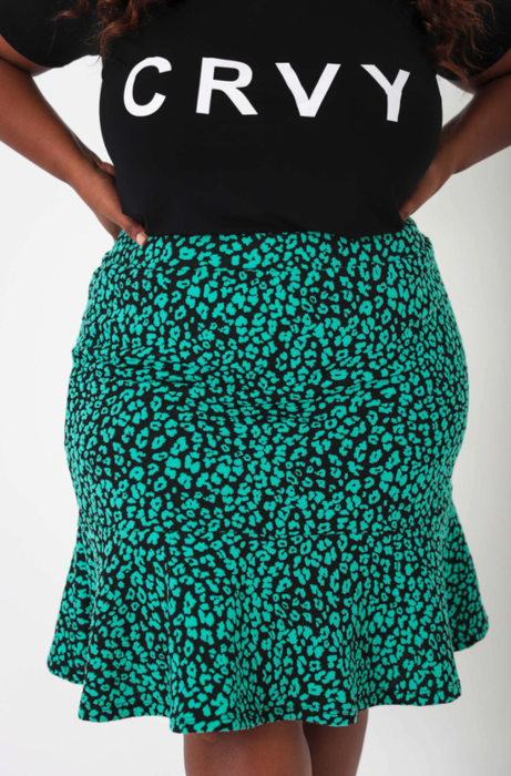 The model is wearing a teal and black leopard print skirt.