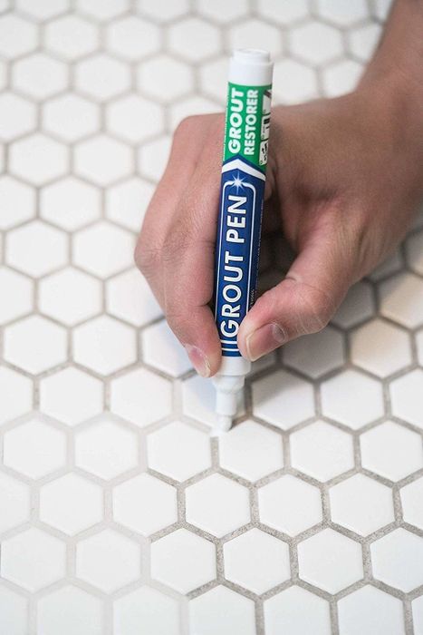 hand holding a marker and applying white paint over brown grout