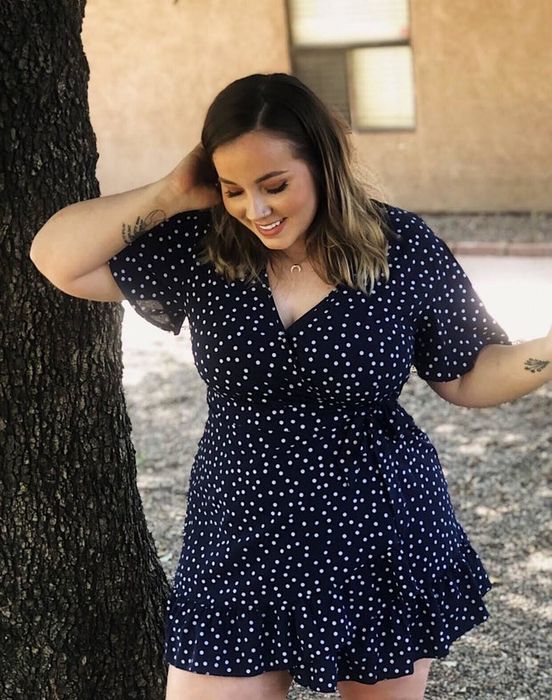 A reviewer is wearing a navy blue dress covered in small white polka dots
