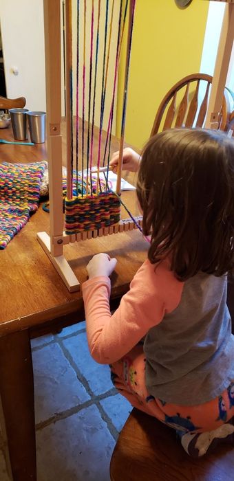 A child from the reviewer's home carefully guiding the wooden needle through the vibrant threads on the loom.
