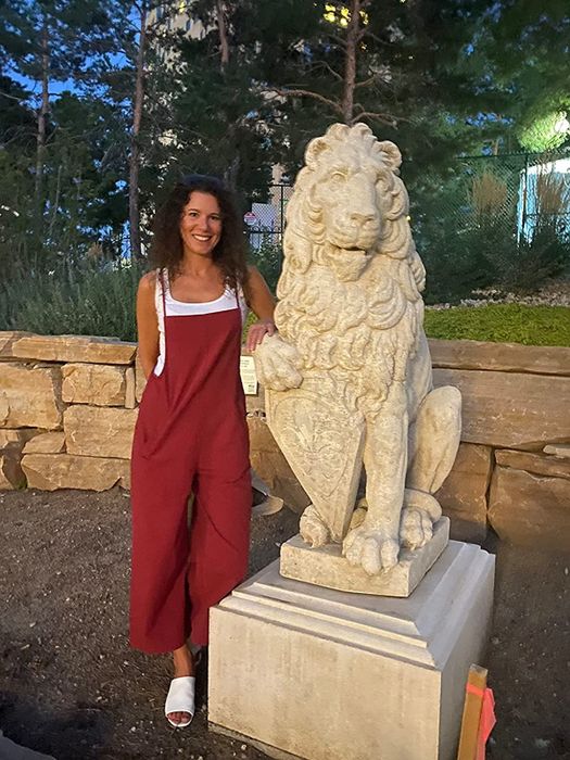 Reviewer wearing red overalls with a white shirt, standing beside a lion statue
