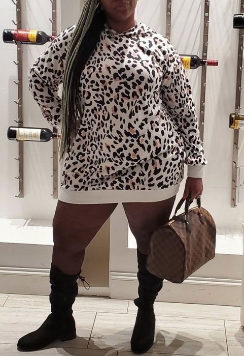 A reviewer rocking a white leopard print sweatshirt dress, paired with black knee-high boots for a bold and stylish combination.
