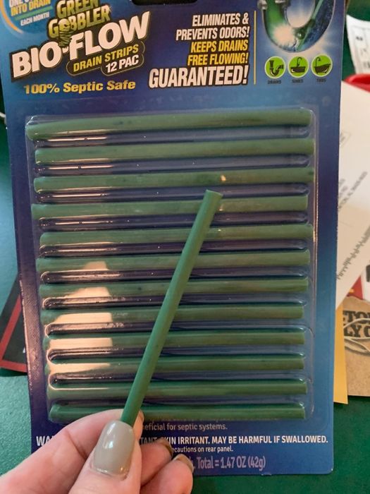A hand holds a green drain deodorizer strip.