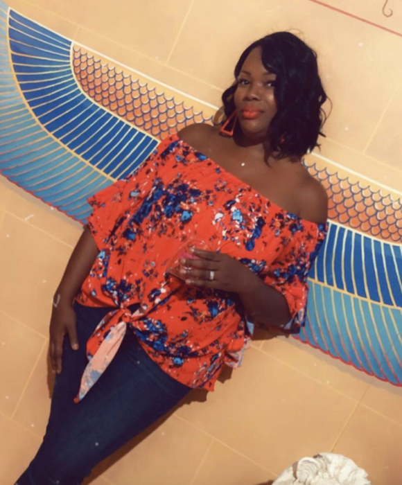 A reviewer is seen wearing a red off-shoulder top with a beautiful floral design.
