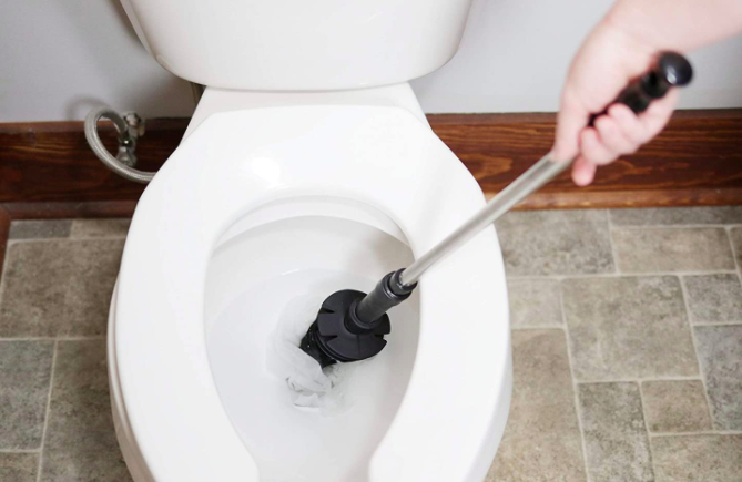 A hand holds the black and silver ToiletShroom, unclogging a toilet with ease.