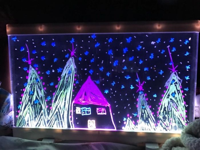 A reviewer's photo showing their child's artwork glowing on the light board