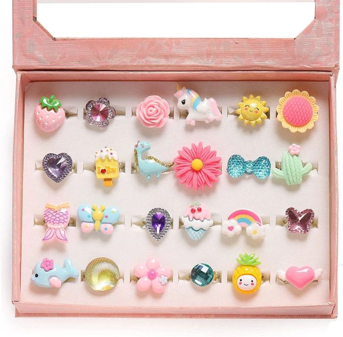 A pink box containing 24 rings in fun shapes like dinosaurs, strawberries, bows, cacti, pineapples, and more.