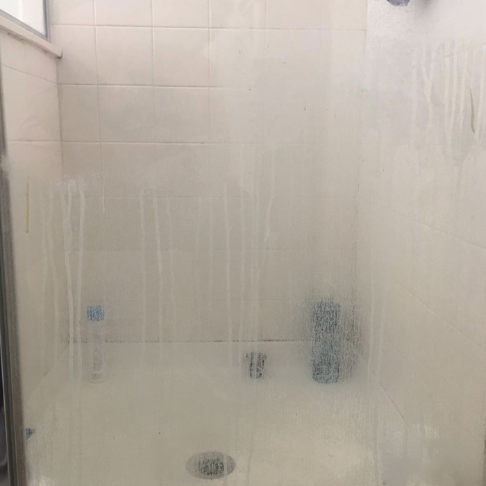 The reviewer's shower door before using the all-purpose power scrubber cleaning kit, covered in hard water stains.