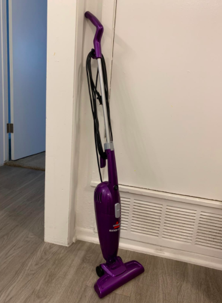 A dark purple Bissell lightweight vacuum stands upright on a hardwood floor.