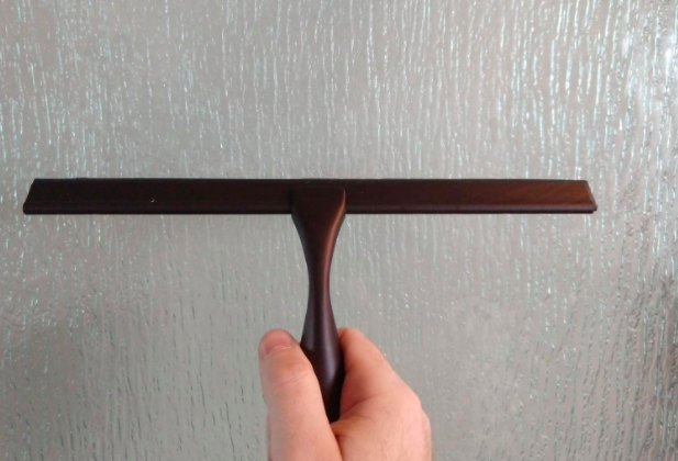 A reviewer uses a brown squeegee to eliminate hard water stains from their shower door.